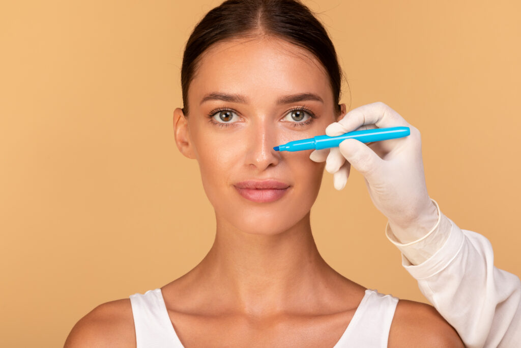 Doctor making marks on patient's face, young caucasian lady on consultation at surgeon