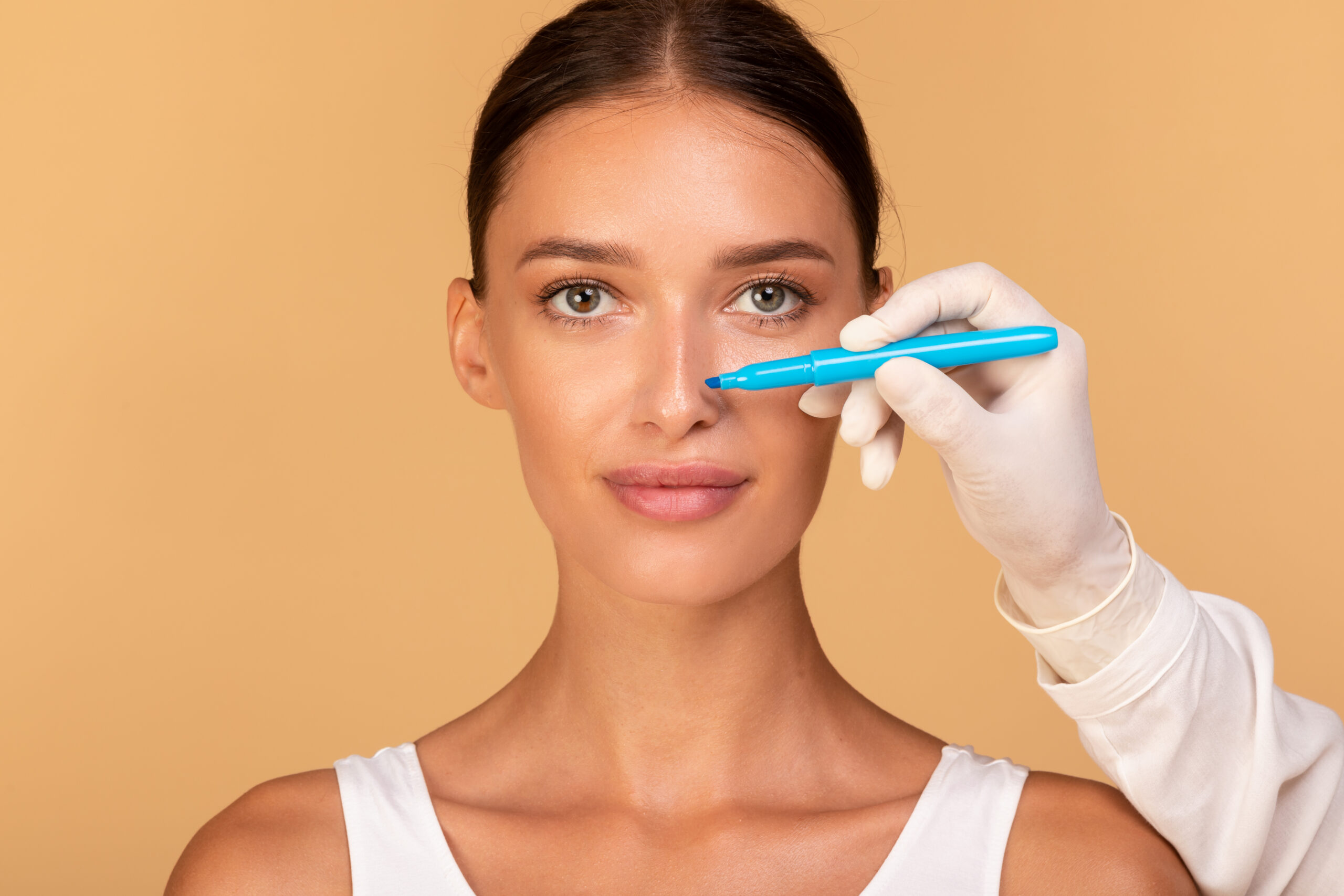 Doctor making marks on patient's face, young caucasian lady on consultation at surgeon