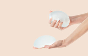 Female hands holding and squeezing soft round breast implants. Plastic surgery